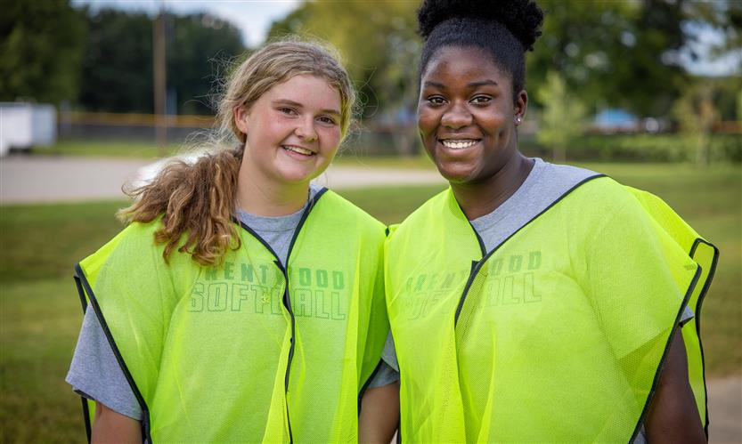 Two girls smile while wearing neon vests